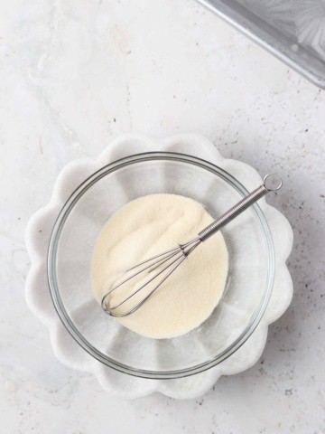 Gelatin and water in a glass mixing bowl with a small whisk.