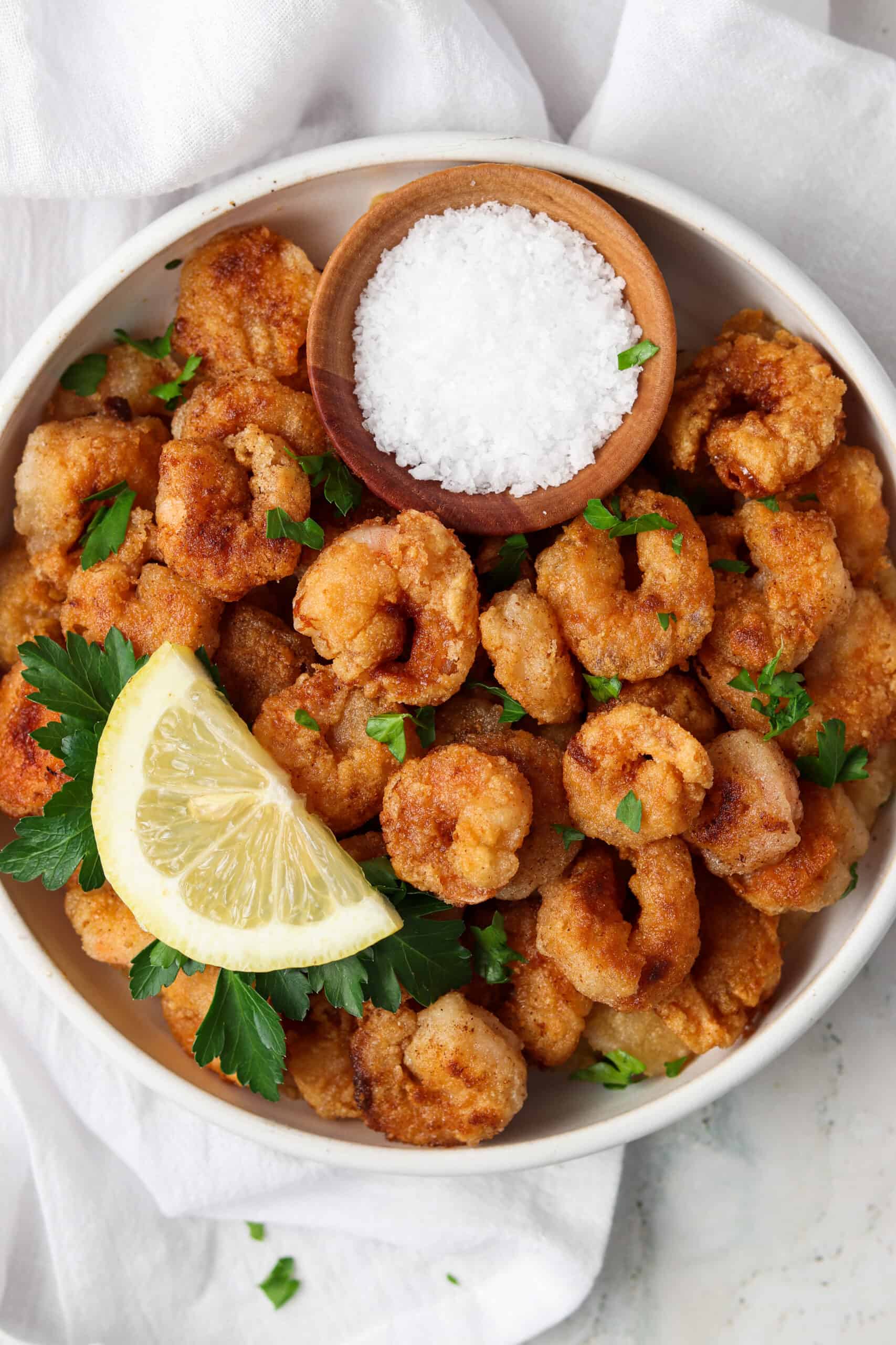 Gluten free crispy shrimp on a white plate with lemons and fresh parsley.