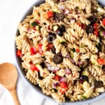 Pasta salad with olives, peppers and onions in a blue bowl with a white napkin under it.