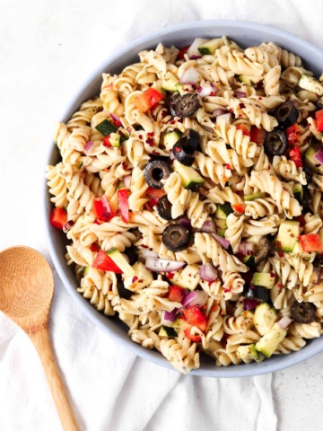 Pasta salad with olives, peppers and onions in a blue bowl with a white napkin under it.