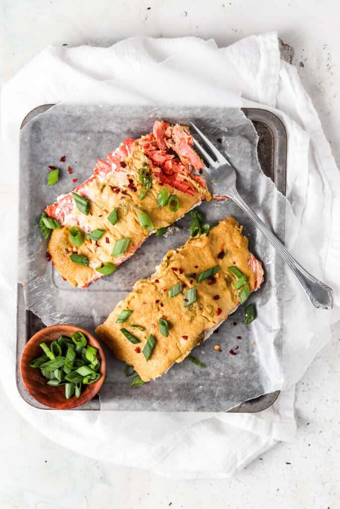 herb crusted salmon on an oven tray with green onions and red pepper