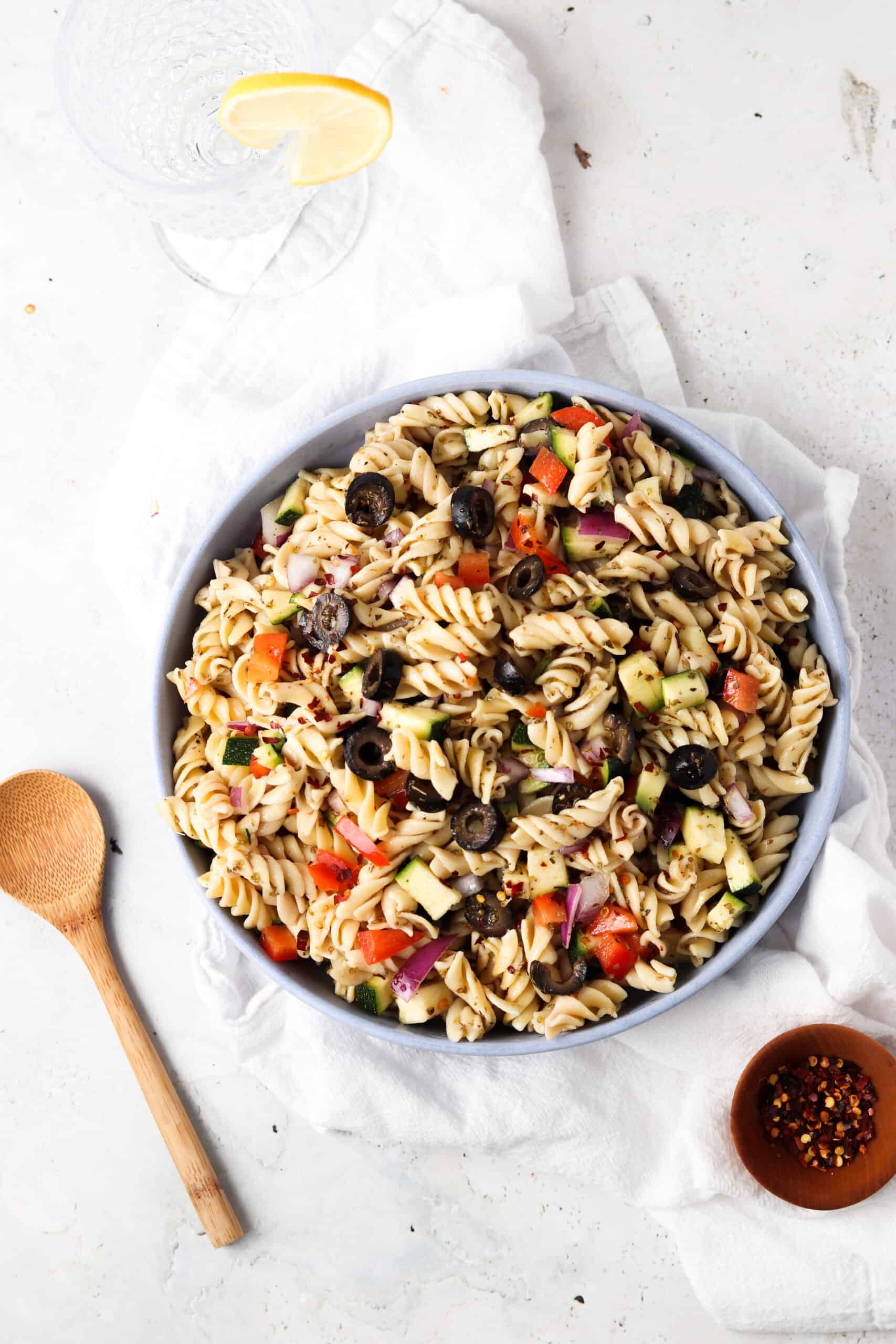 Paleo pasta salad in a blue bowl with a glass and red pepper flakes.