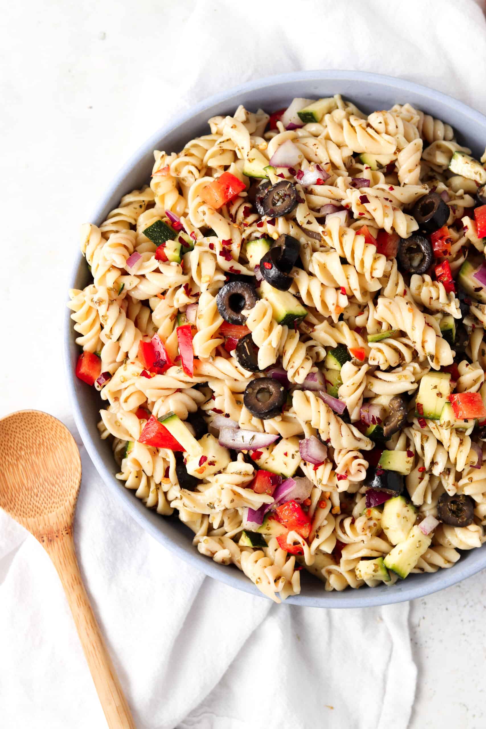 Paleo pasta salad in a blue bowl with a wooden spoon.