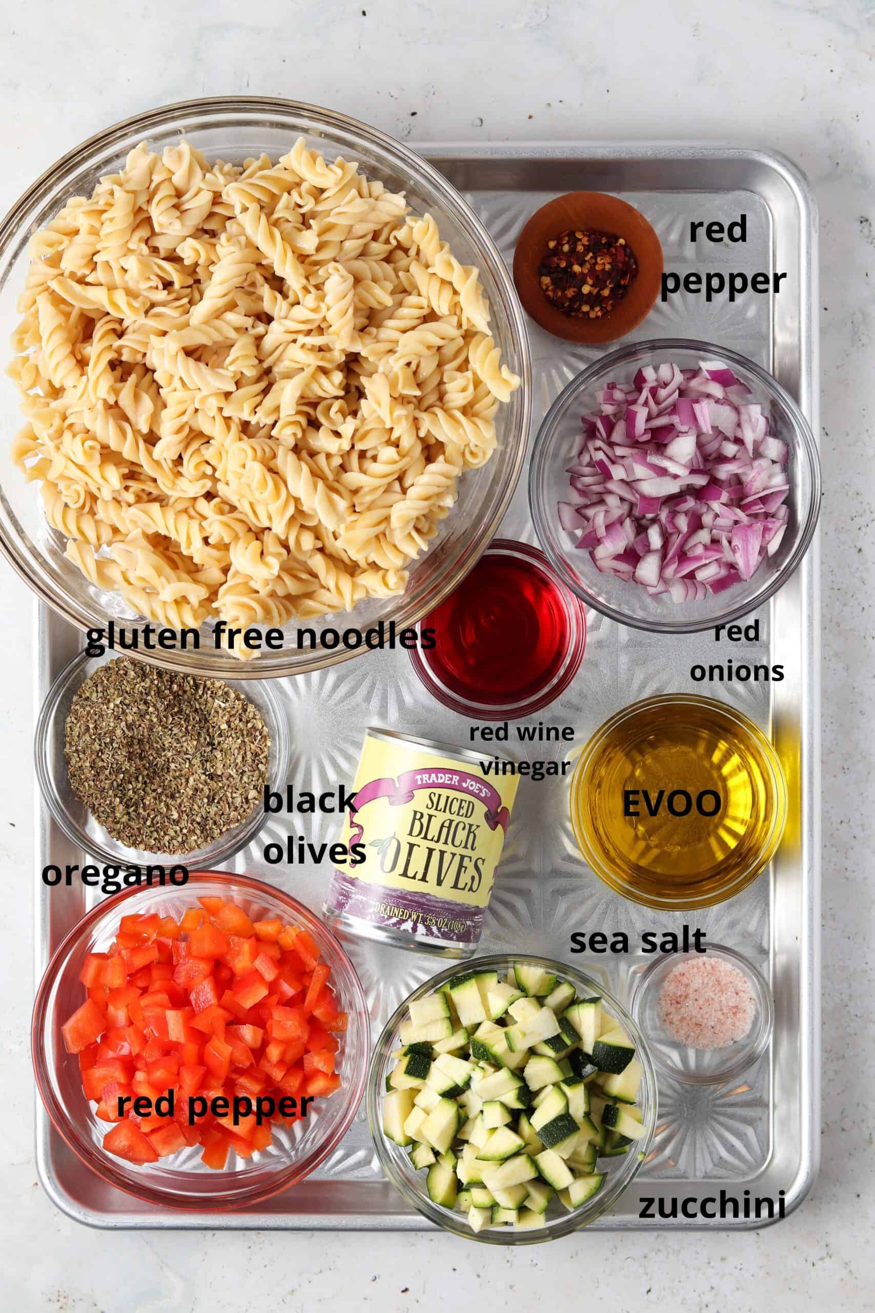 Paleo pasta salad ingredients in glass mixing bowls on a metal tray.