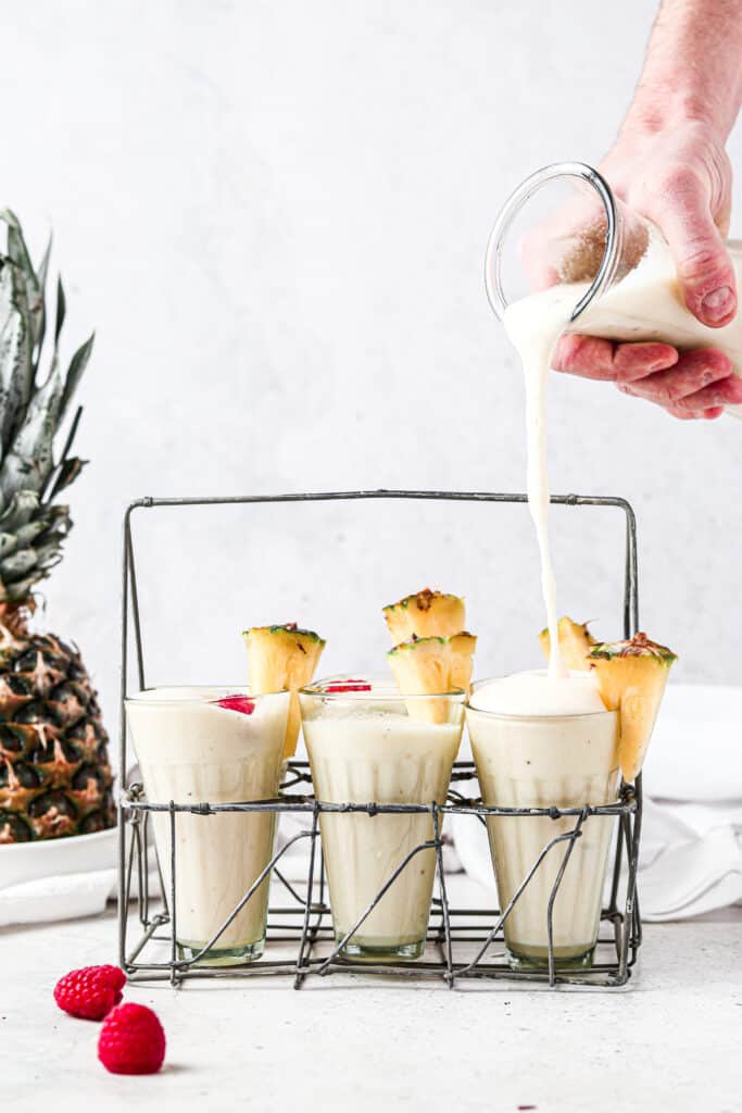 man pouring paleo pina colada into a glass with 6 other glasses