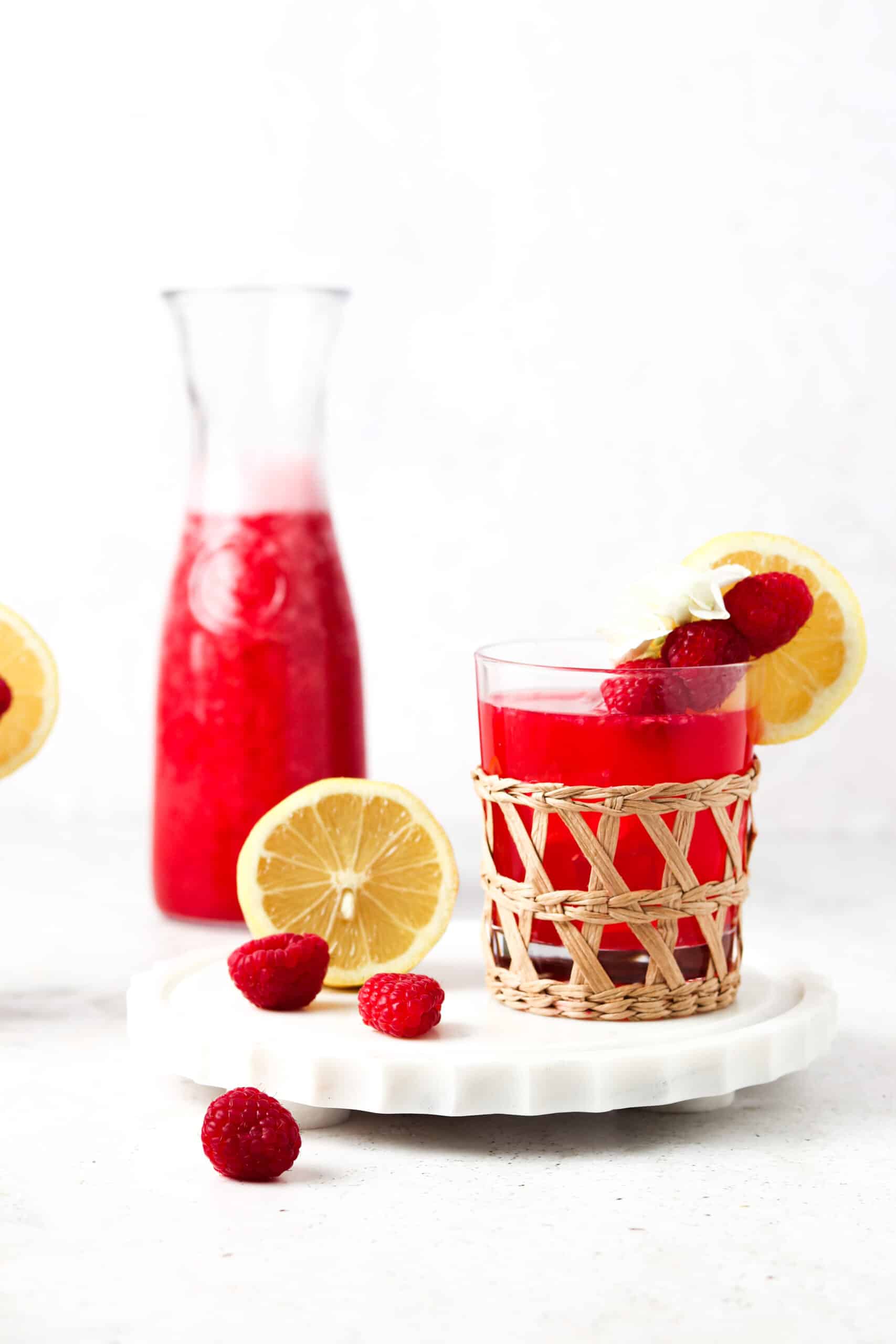 Paleo raspberry lemonade in a clear glass with lemon garnishes.