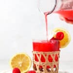 Raspberry lemonade poured into a basket weaved glass with on a marble plate.