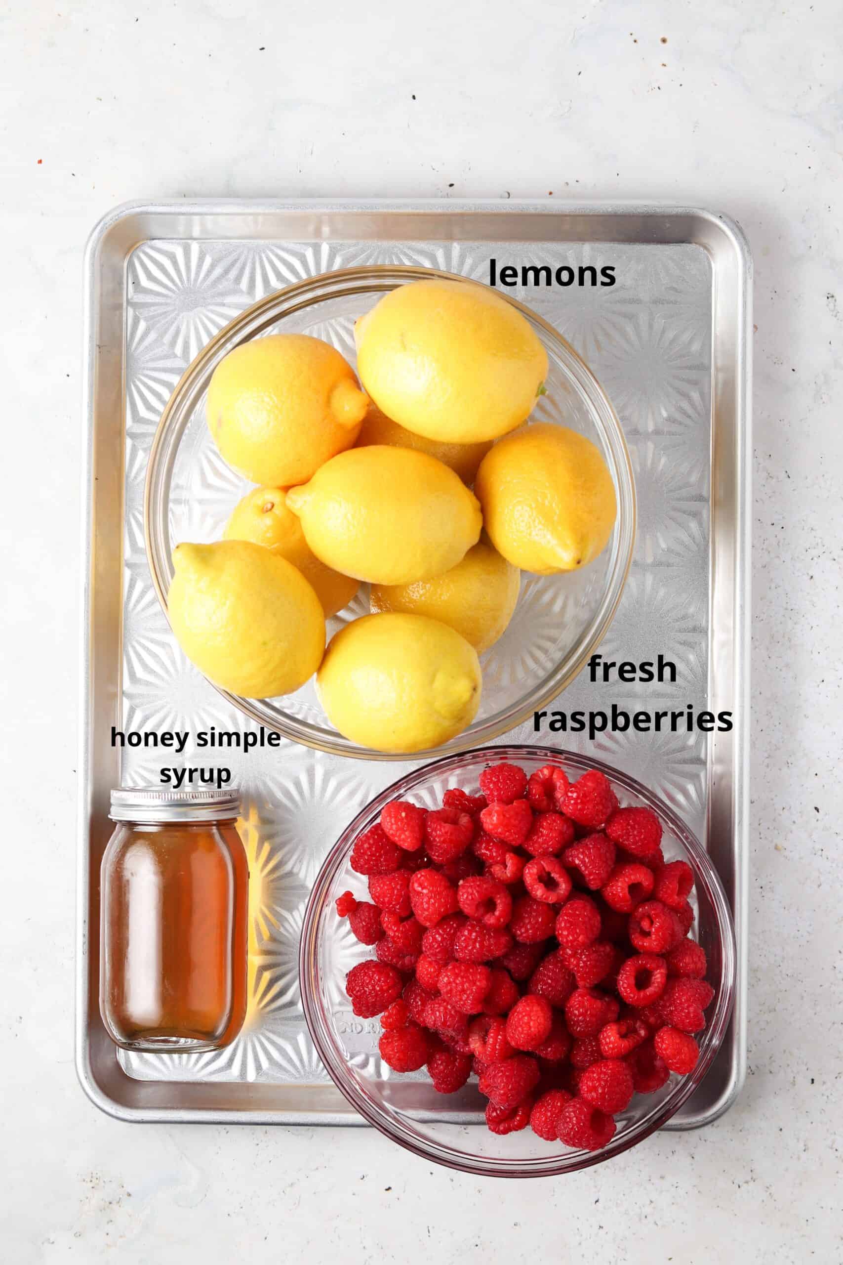 Lemonade ingredients laid out in glass bowls on a metal sheet pan.