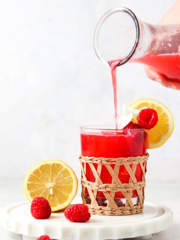 Raspberry lemonade poured in a whicker cup on a marble plate with berries on the side.
