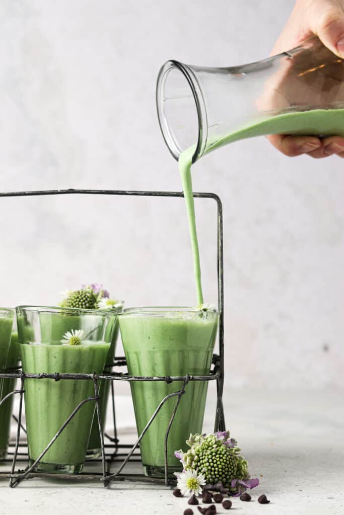mint smoothie in a smoothie jar with someone pouring more smoothie in