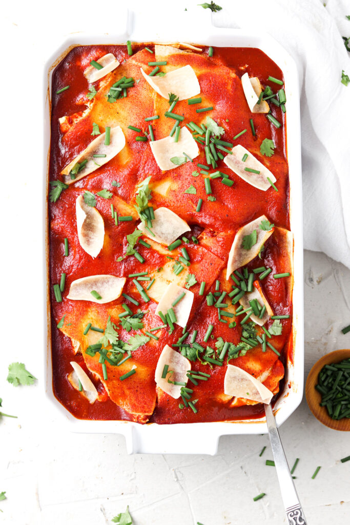 paleo mexican lasagna with red sauce in a white casserole dish with cheese and green herbs on top