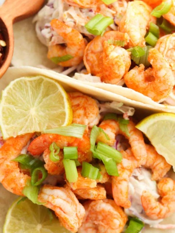 Buffalo marinated shrimp on tortilla shells with slaw and limes on top.