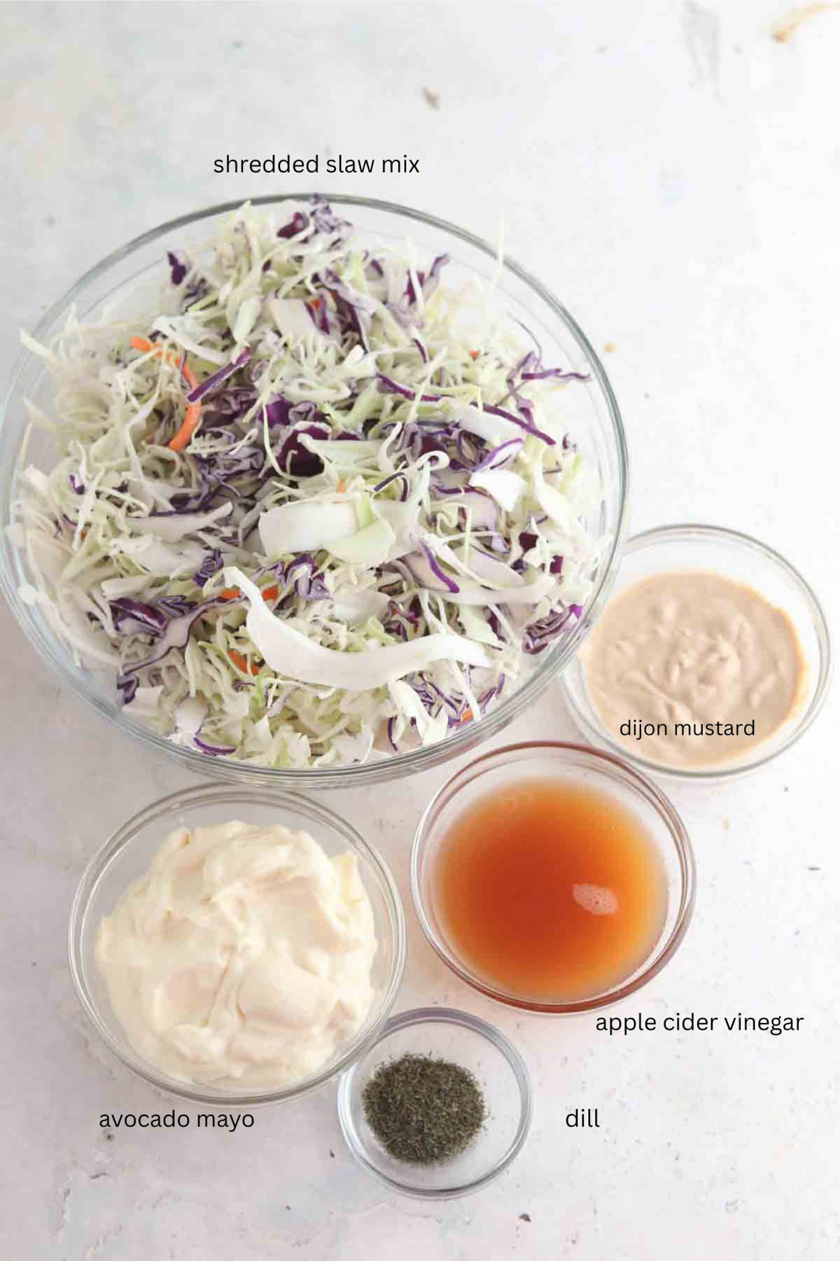 Creamy coleslaw ingredients laid out in small glass bowls on the counter. 