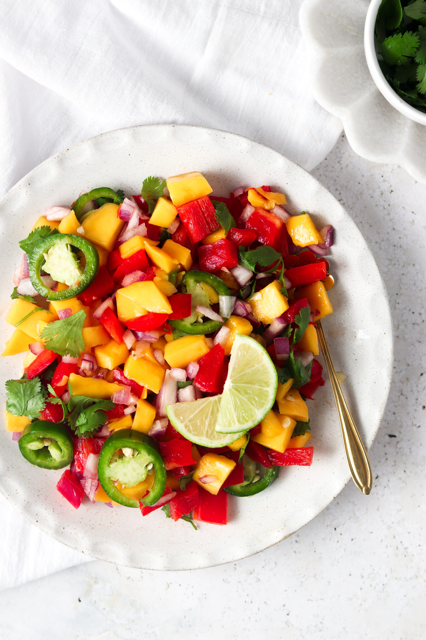 Mango pico de gallo in a white bowl with a gold spoon. 