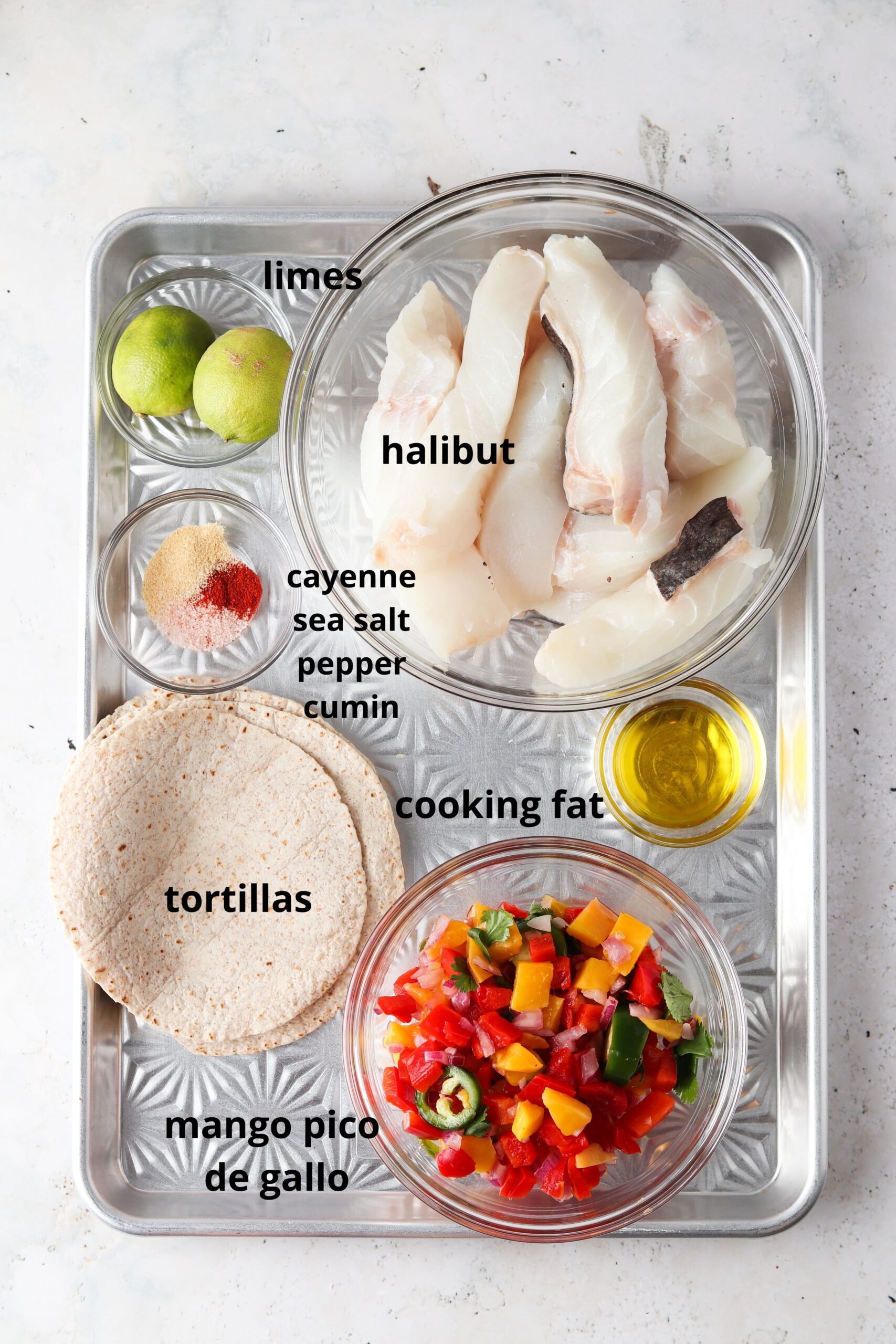 Halibut fish taco ingredients in glass bowls on a silver tray. 