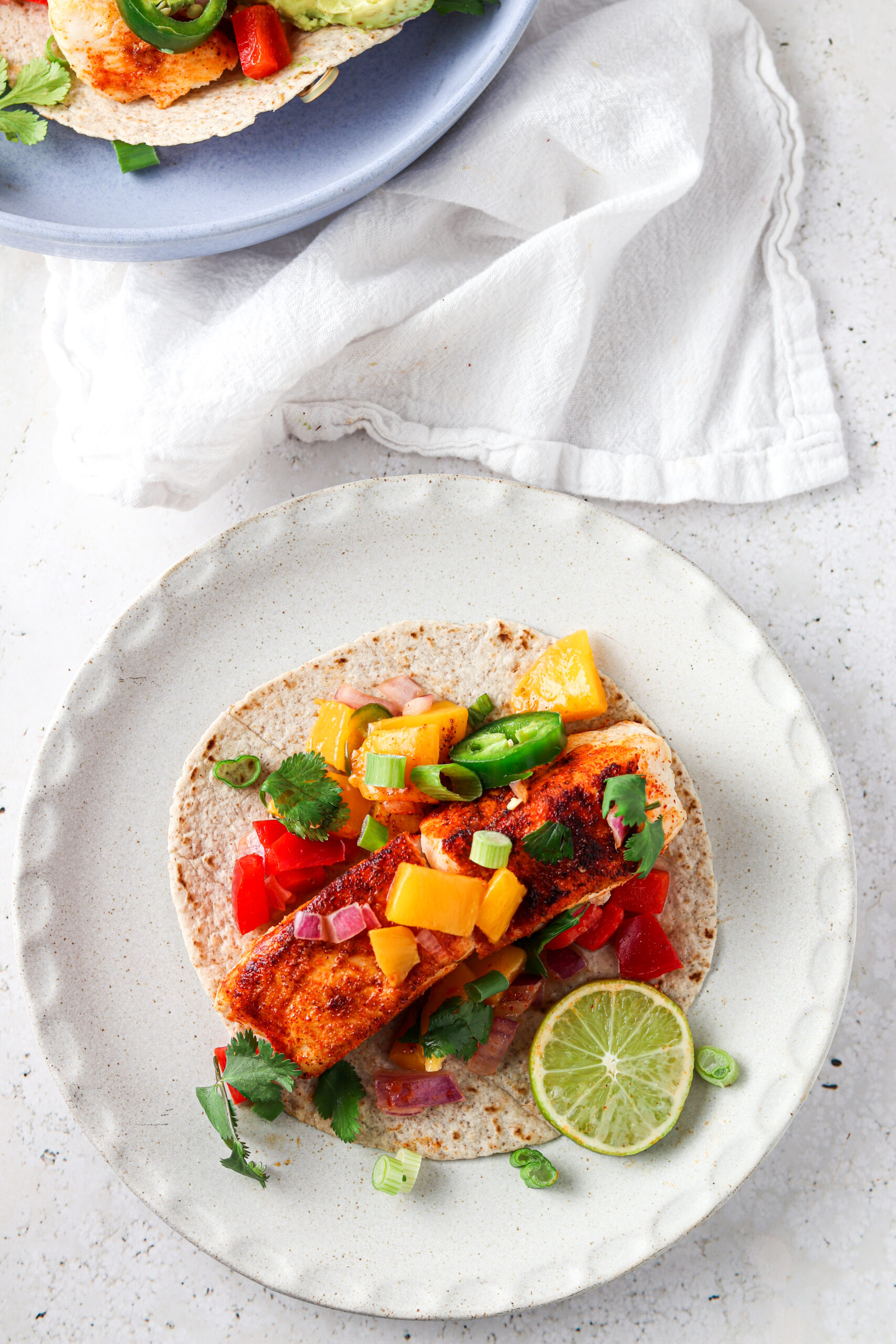 Halibut fish taco on a plate with fresh green herbs and a slice of lime. 