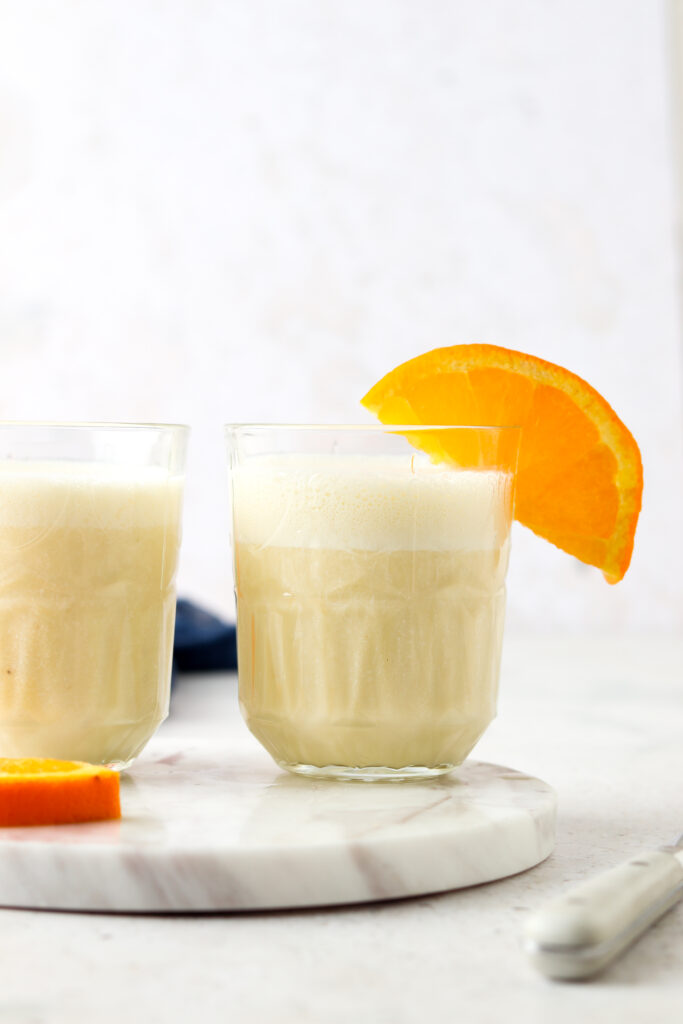 two orange creamsicle smoothies in a glass with oranges on top and a blue napkin