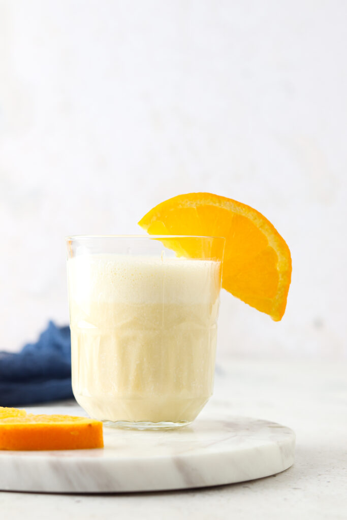 orange creamsicle smoothie in a glass with an orange on it and blue napkin