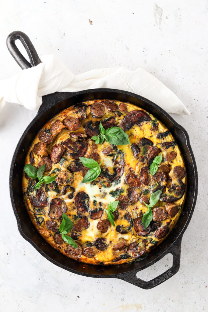 spinach mushroom frittata in a cast iron pan with basil on top