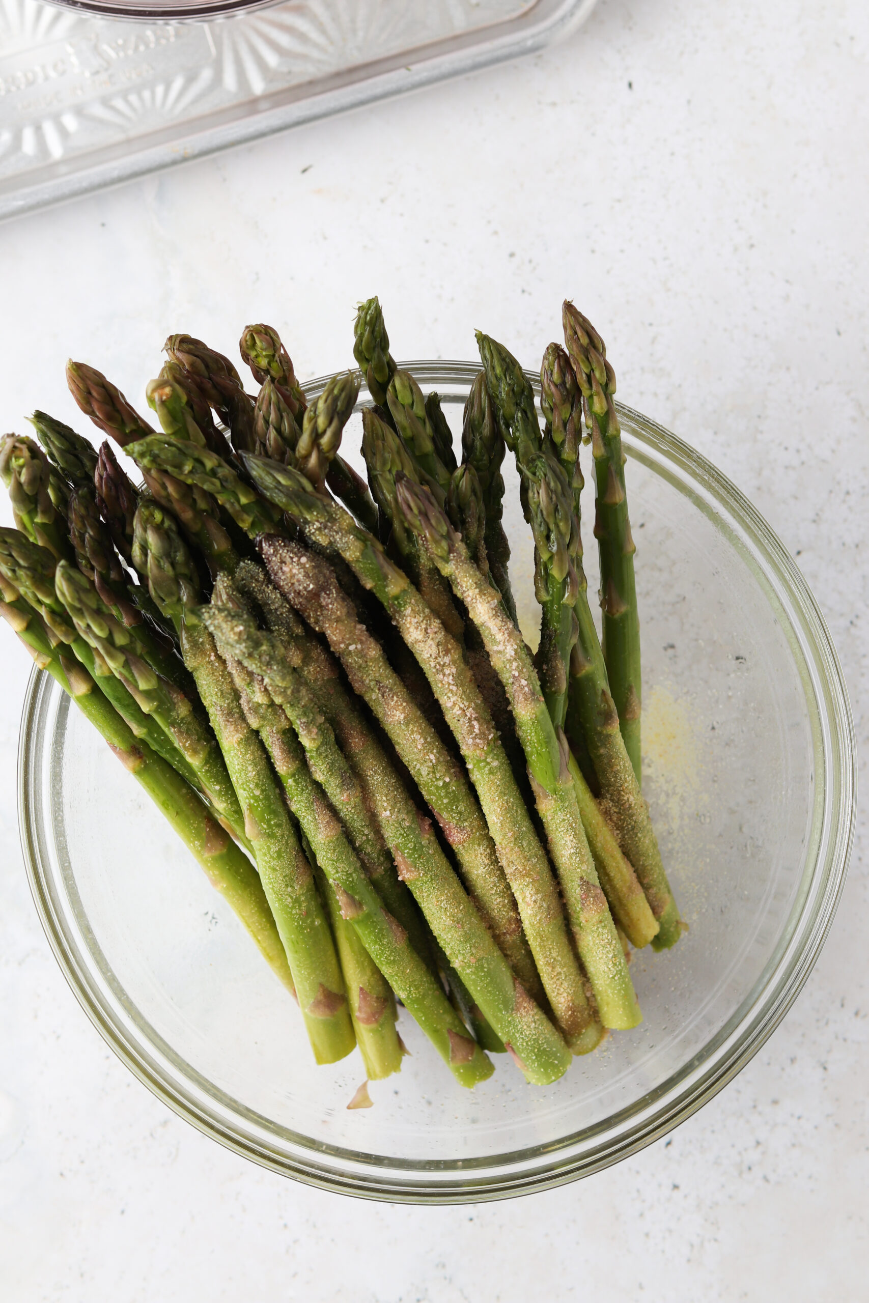 Asparagus in a clear glass bowl with garlic and oil on it. 