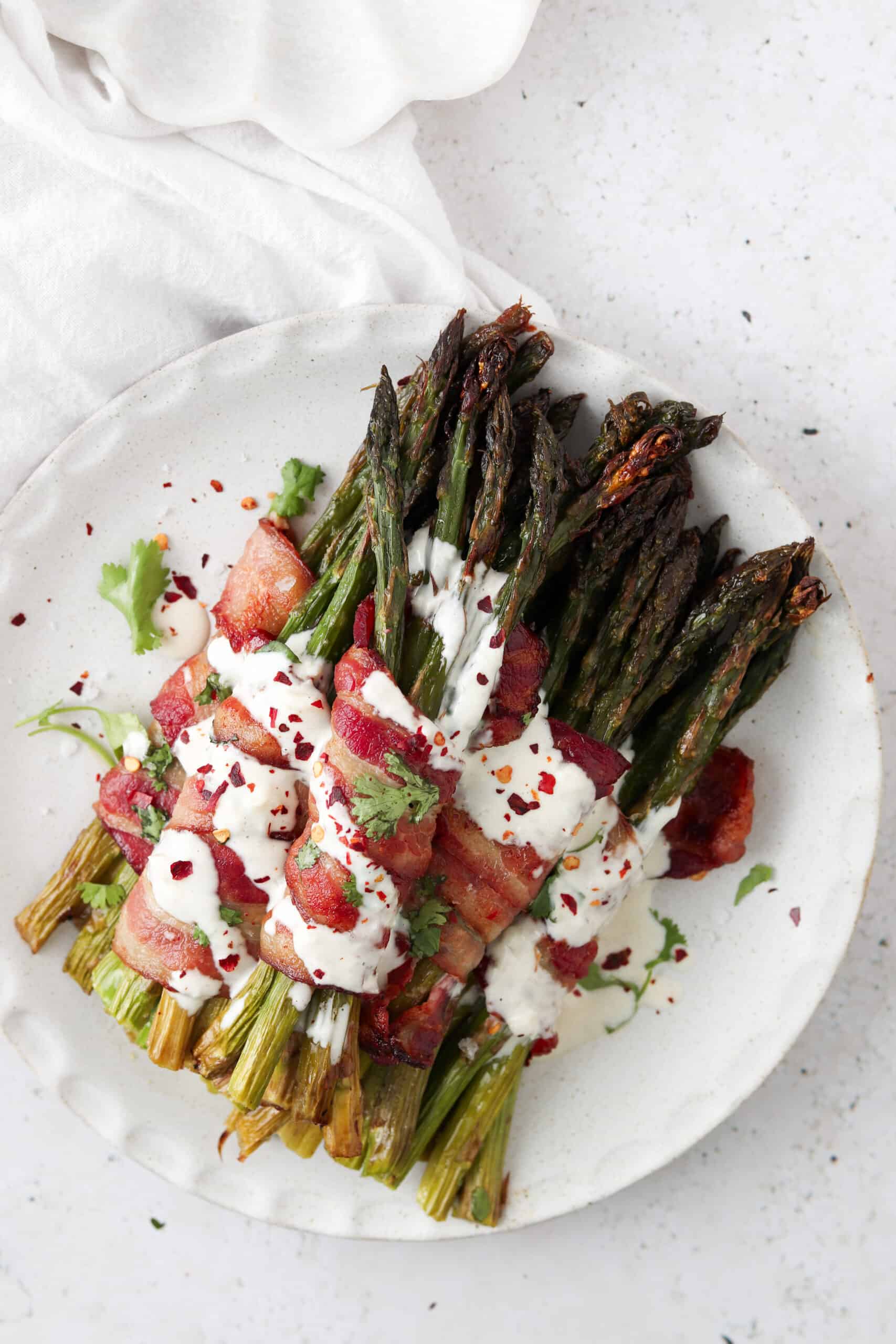 Bacon wrapped asparagus with garlic aioli on a plate with fresh herbs.