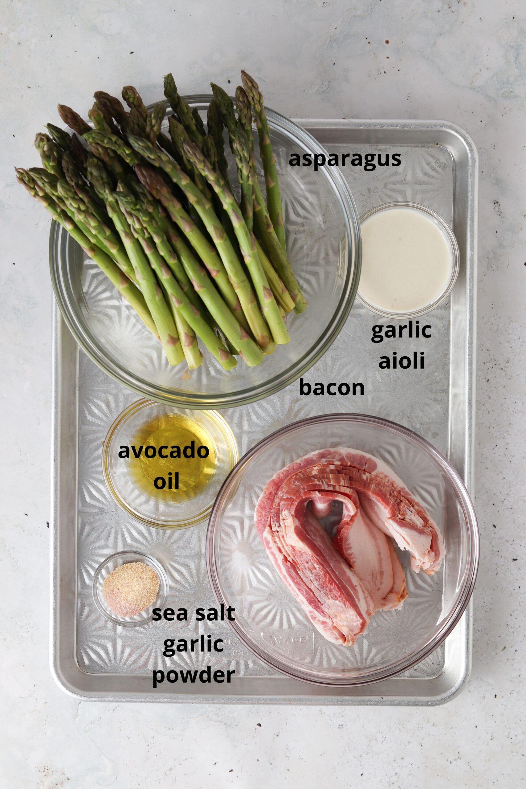Bacon wrapped asparagus ingredients on a tray in glass bowls.