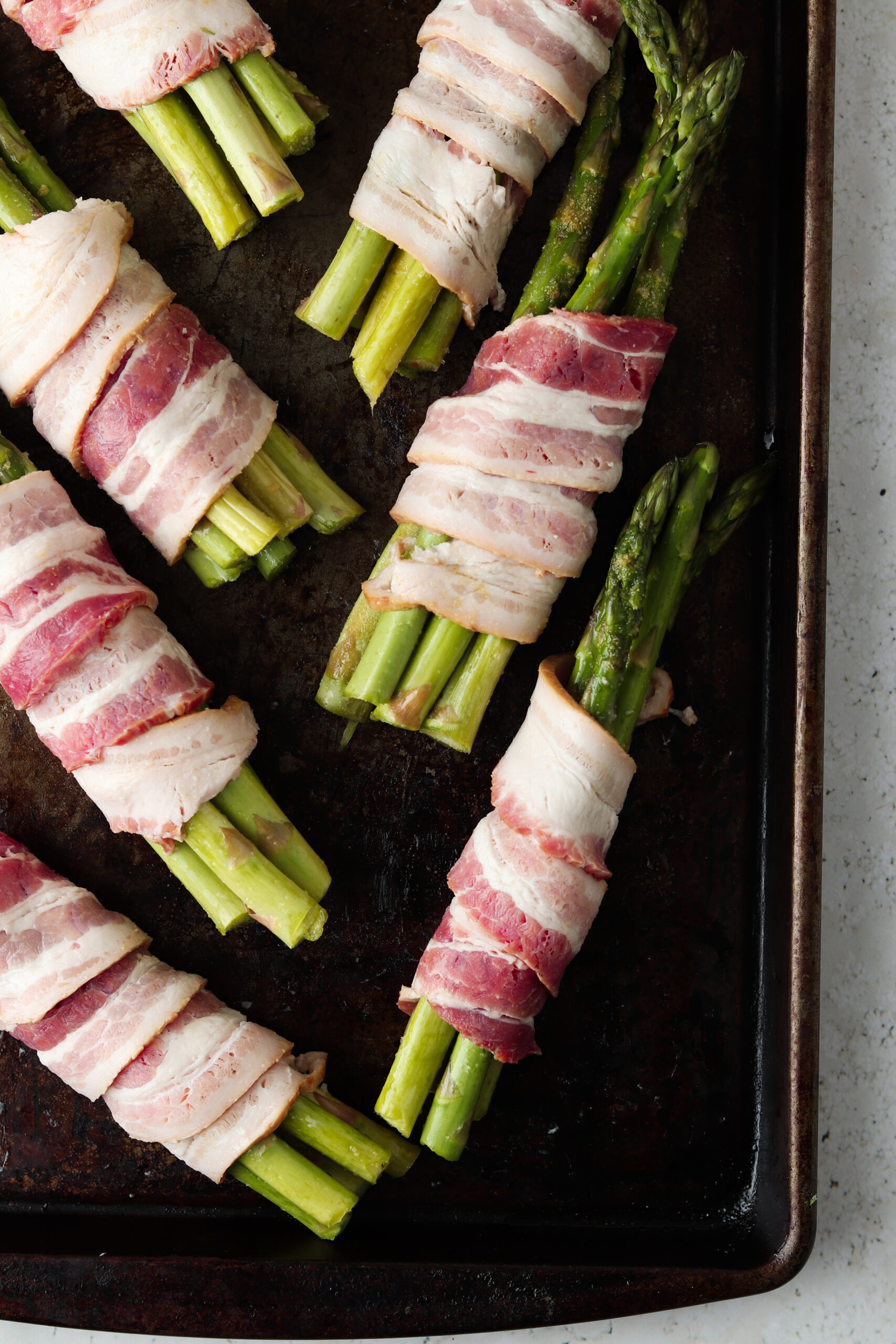 Raw bacon wrapped around bunches of asparagus on a baking sheet. 