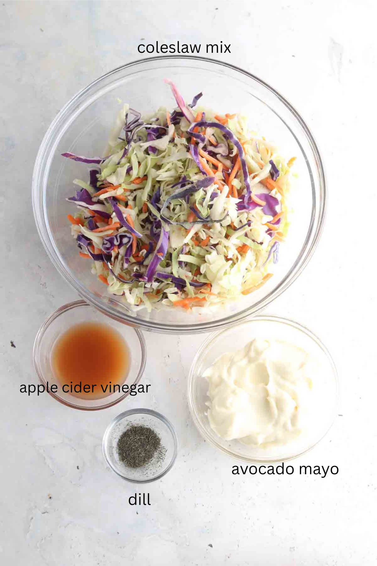 Homemade coleslaw ingredients in glass bowls laid out on the counter. 