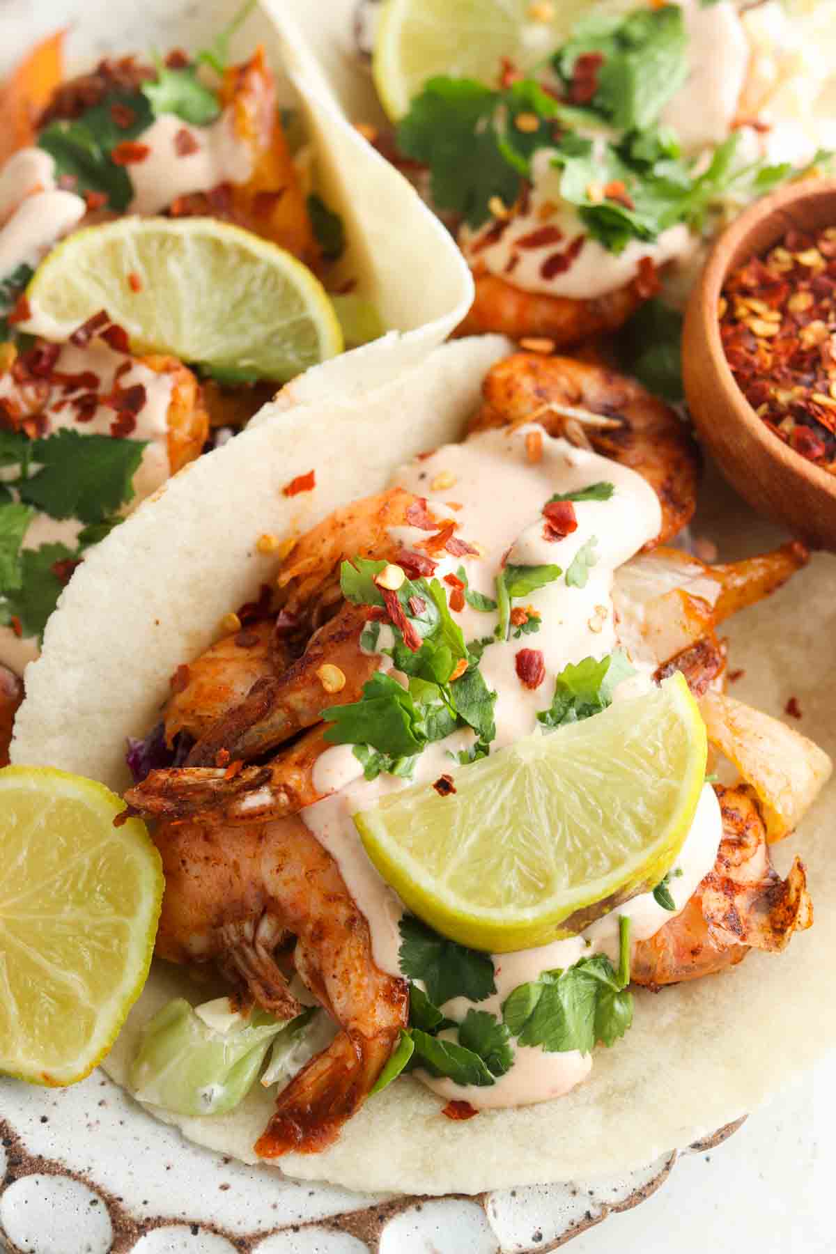 Close up photo of shrimp tacos on a plate with limes, coleslaw and spicy mayo.