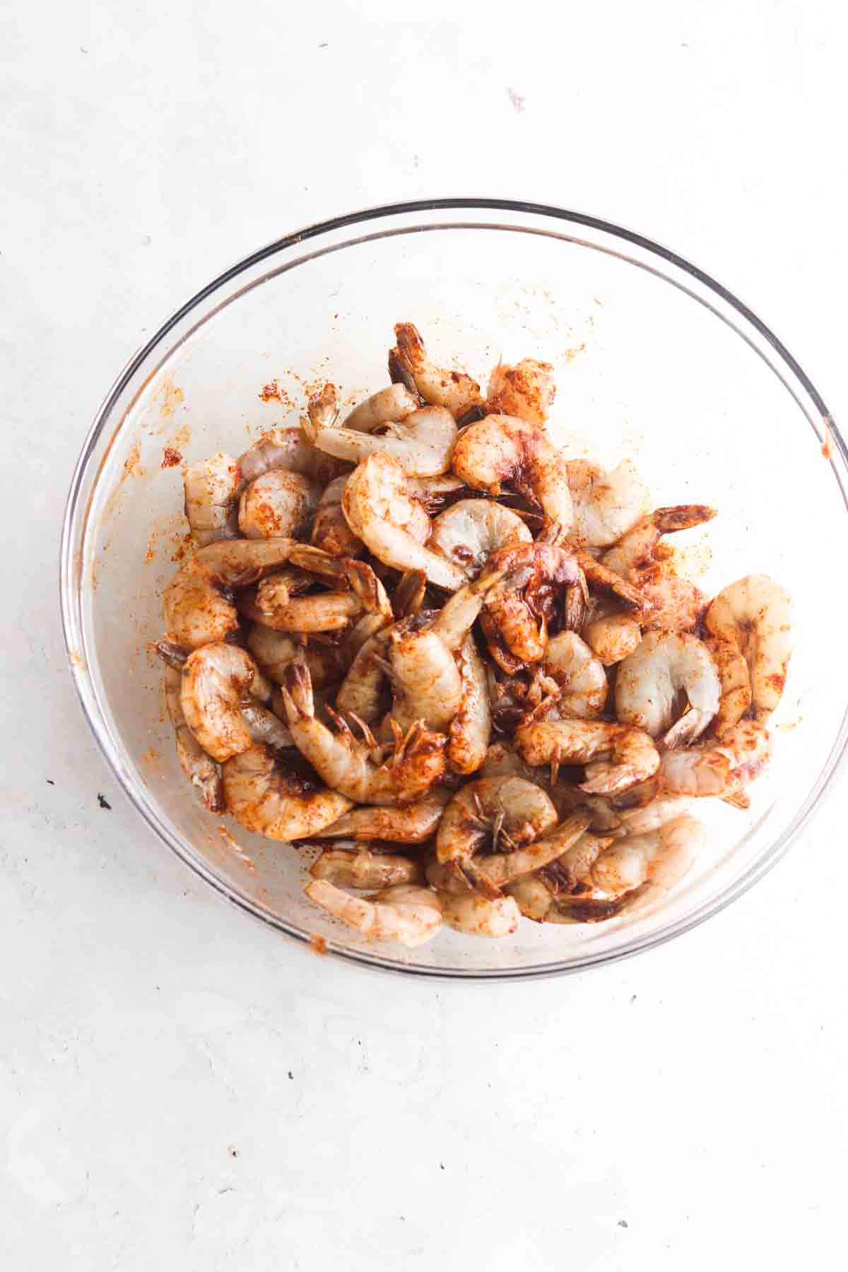 Shrimp, oil and taco seasoning in a large glass bowl.