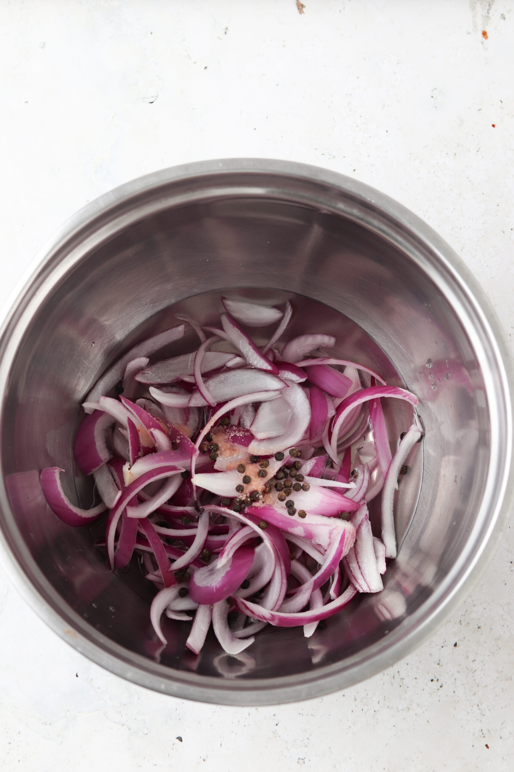 Raw onions and pickling ingredients in a silver bowl.