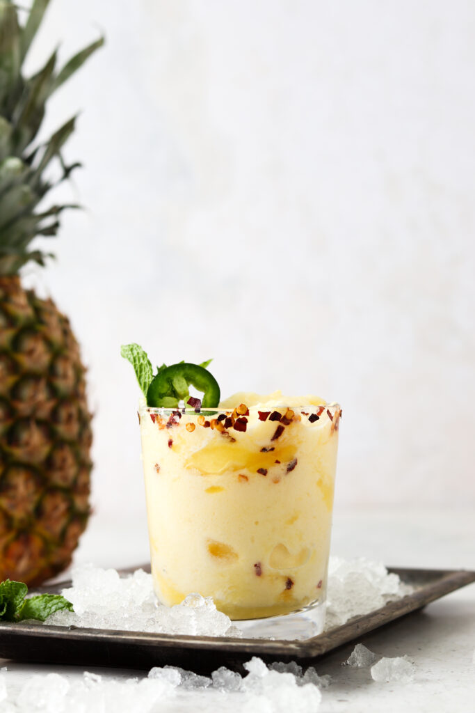 Pineapple margarita on a metal plate with a jalapeno and mint on top.