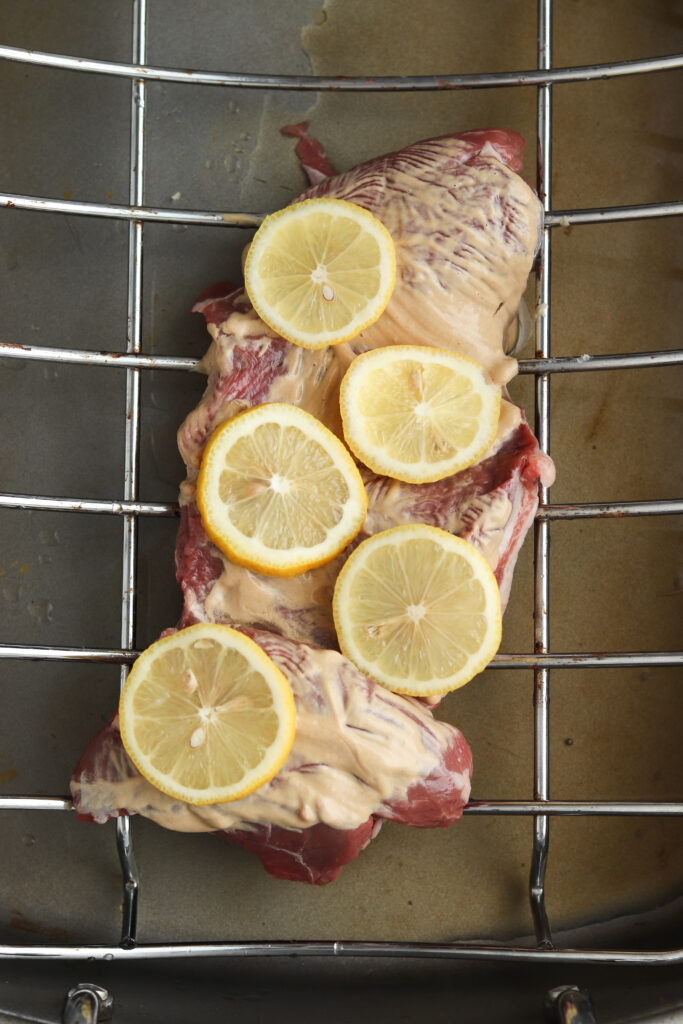 raw lamb on a roasting back with dijon and lemons