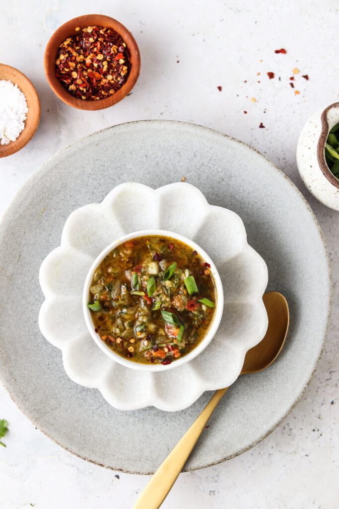 red chimichurri in a bowl with a flower pot and red pepper flakes