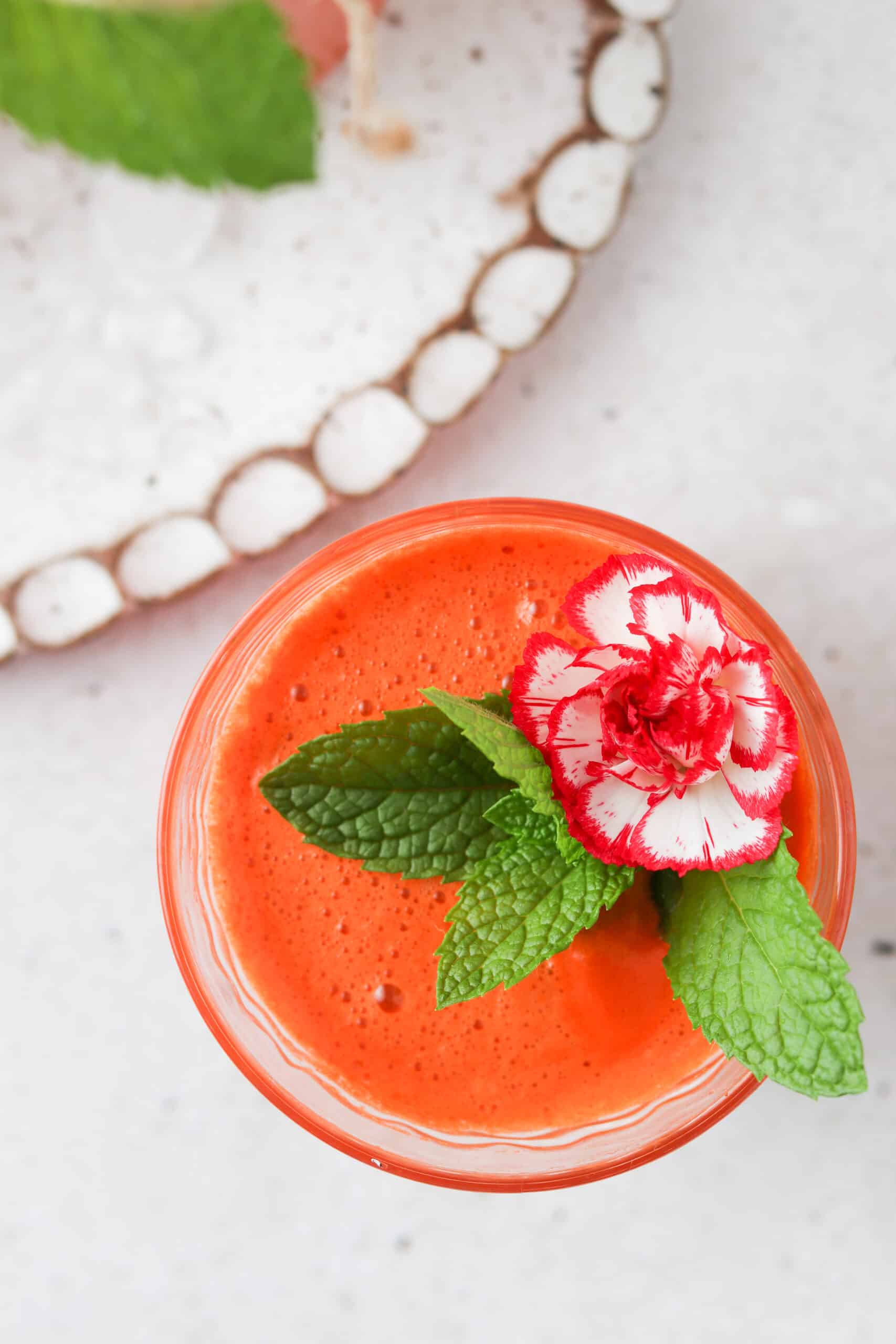 Overhead picture of carrot juice in a glass with a rose and mint on top.