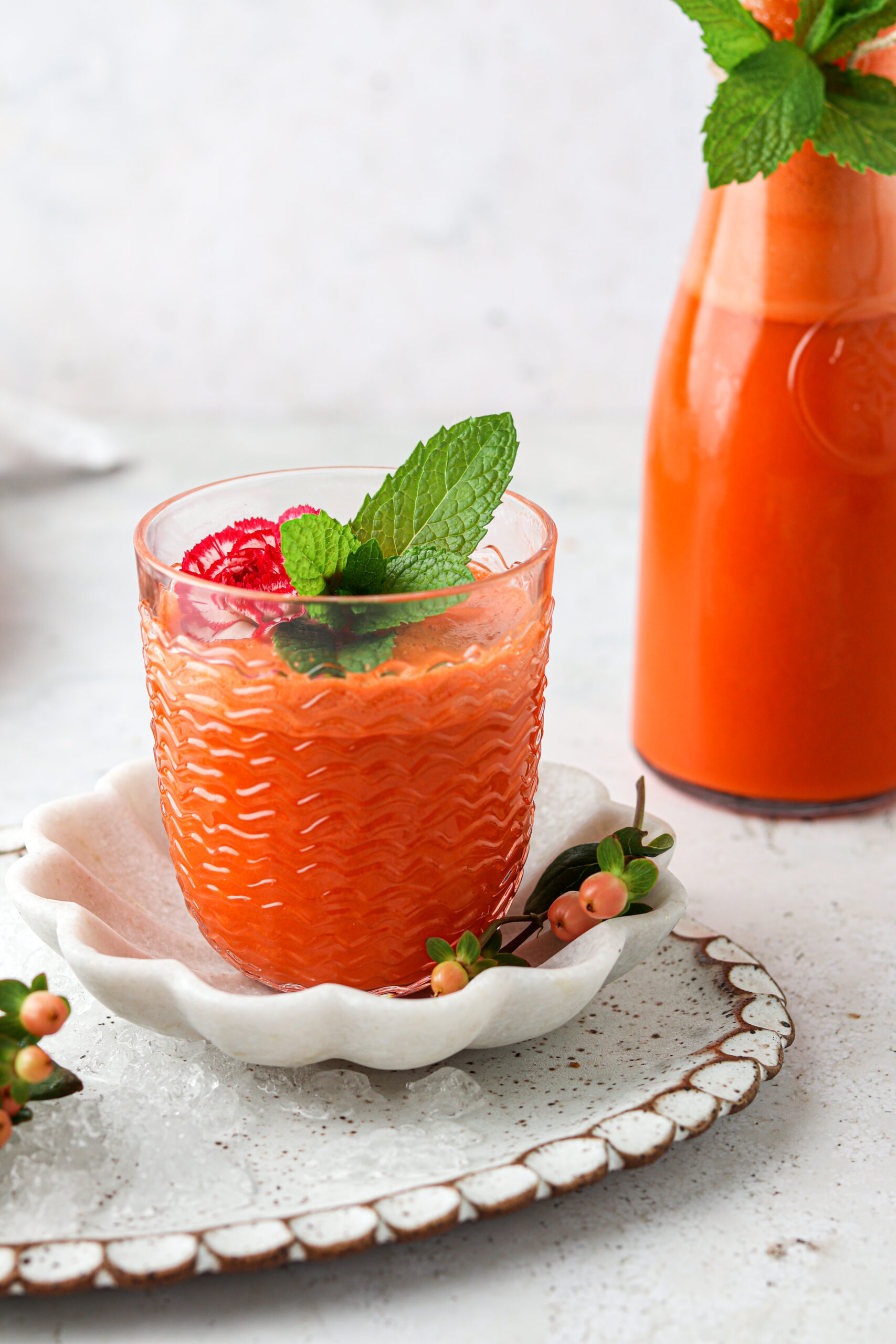 Picture of carrot juice with fresh mint and flowers on top.