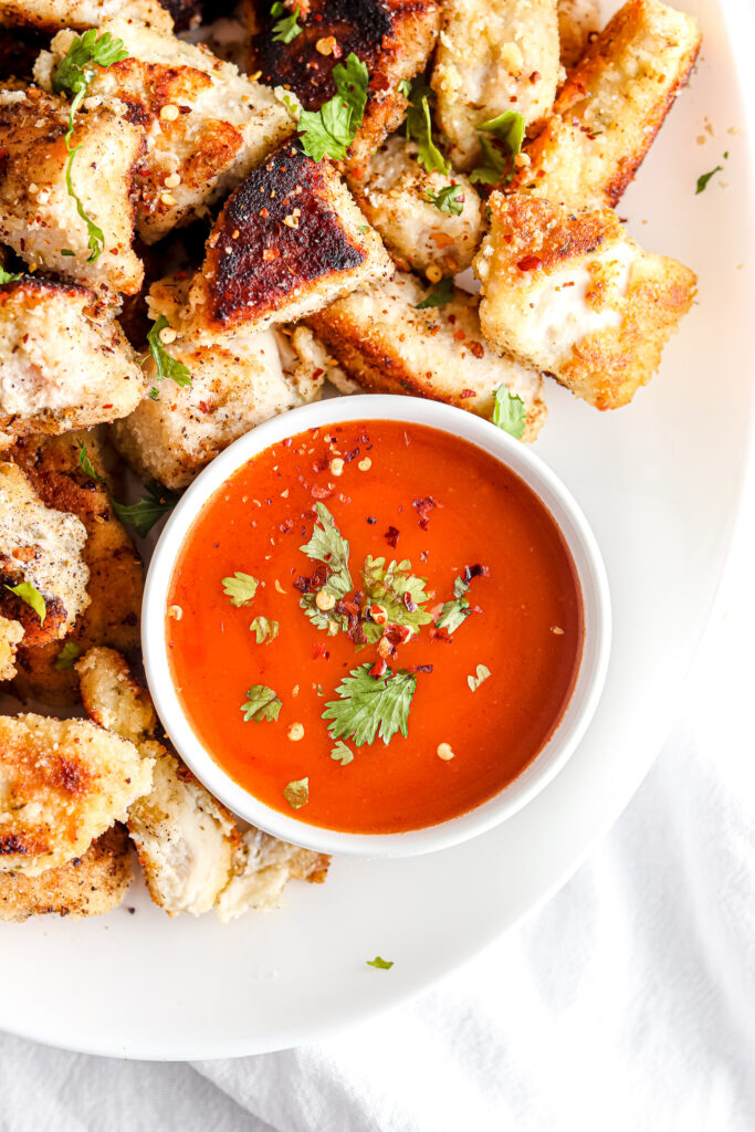 paleo chicken nuggets with buffalo chicken sauce on white plate with parsley garnish