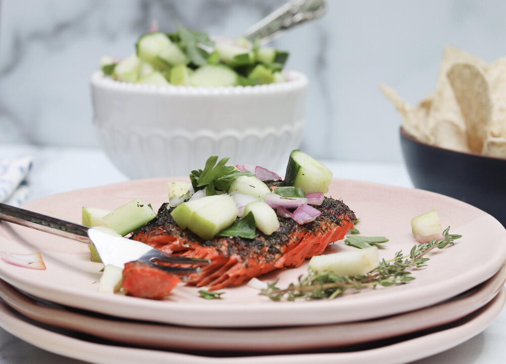 apple cucumber salsa over salmon on a light pink plate with thyme garnish and side of chips