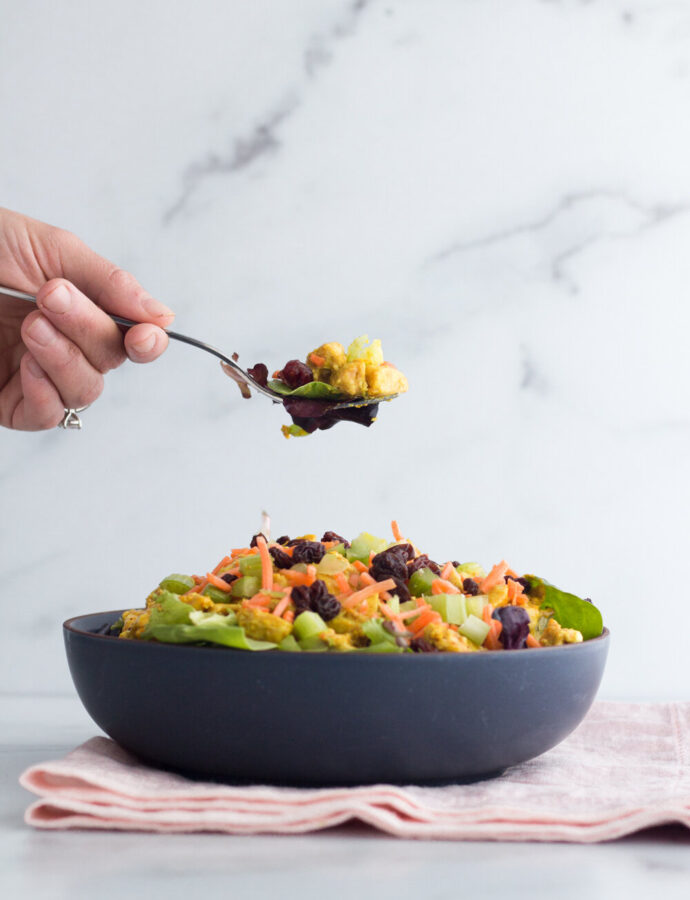 curry chicken salad over greens in a dark bowl sitting on a pale pink towel