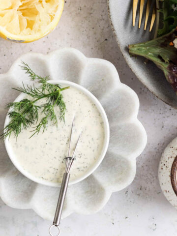 Dill aioli in a small bowl on a scalloped plate.