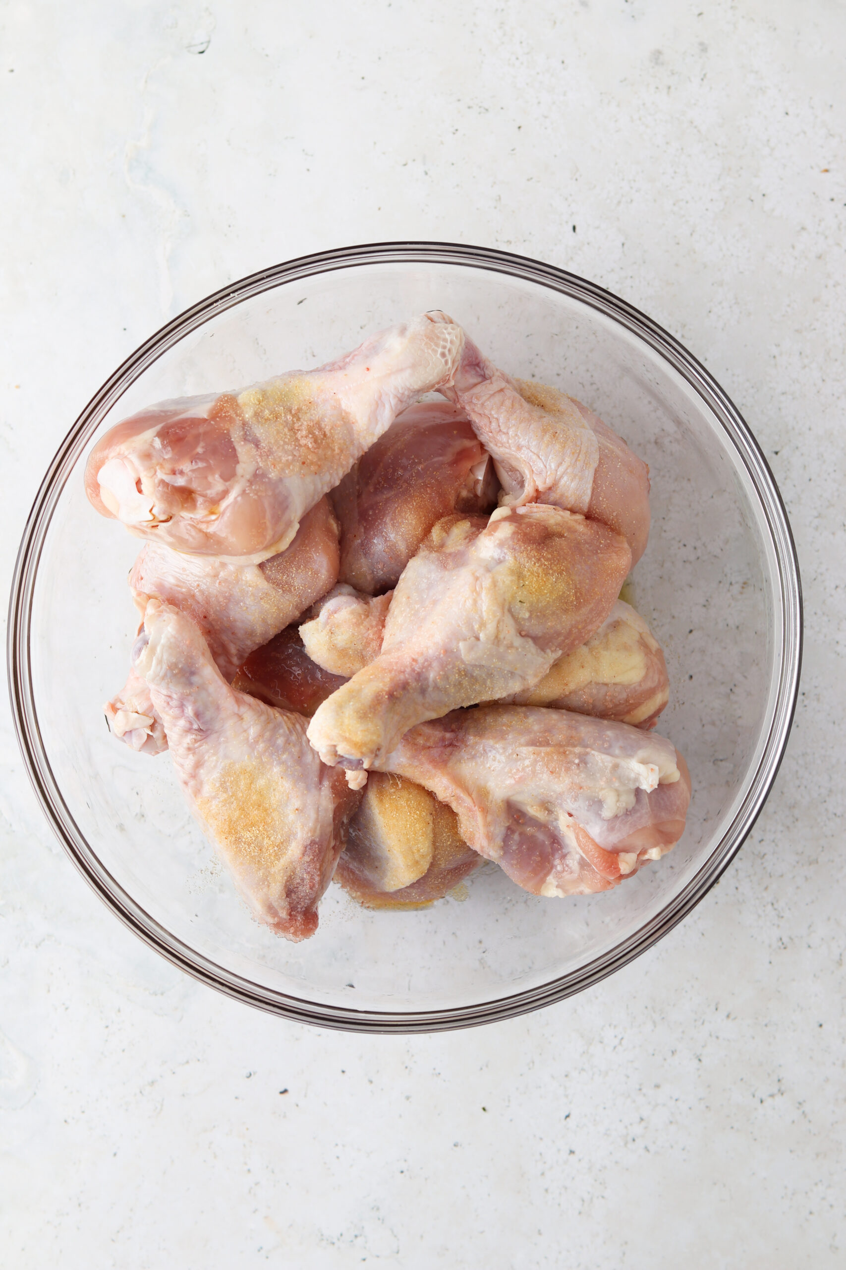 Raw chicken drumsticks in a glass bowl. 