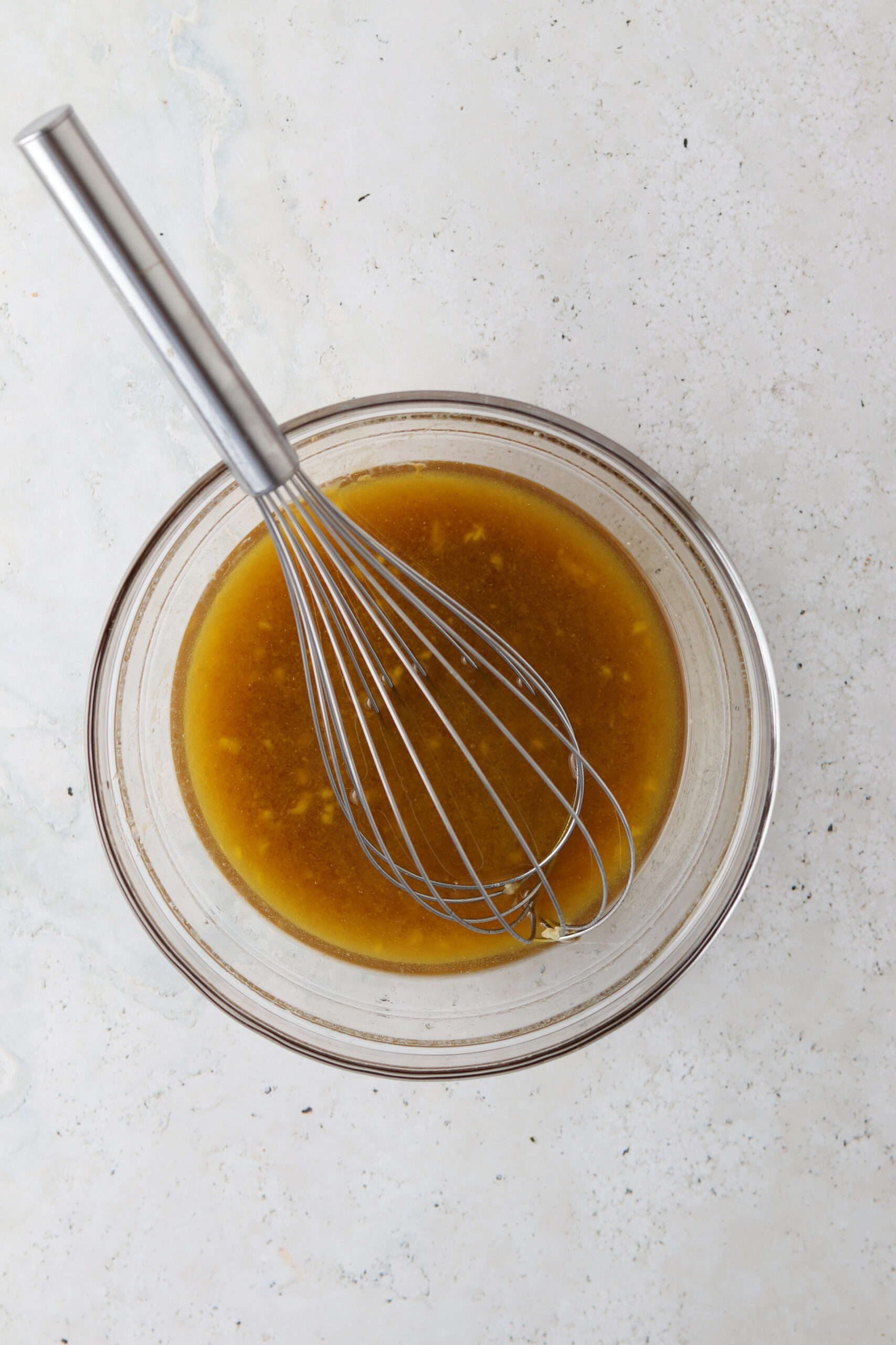 Honey lemon sauce in a small glass bowl with a whisk.