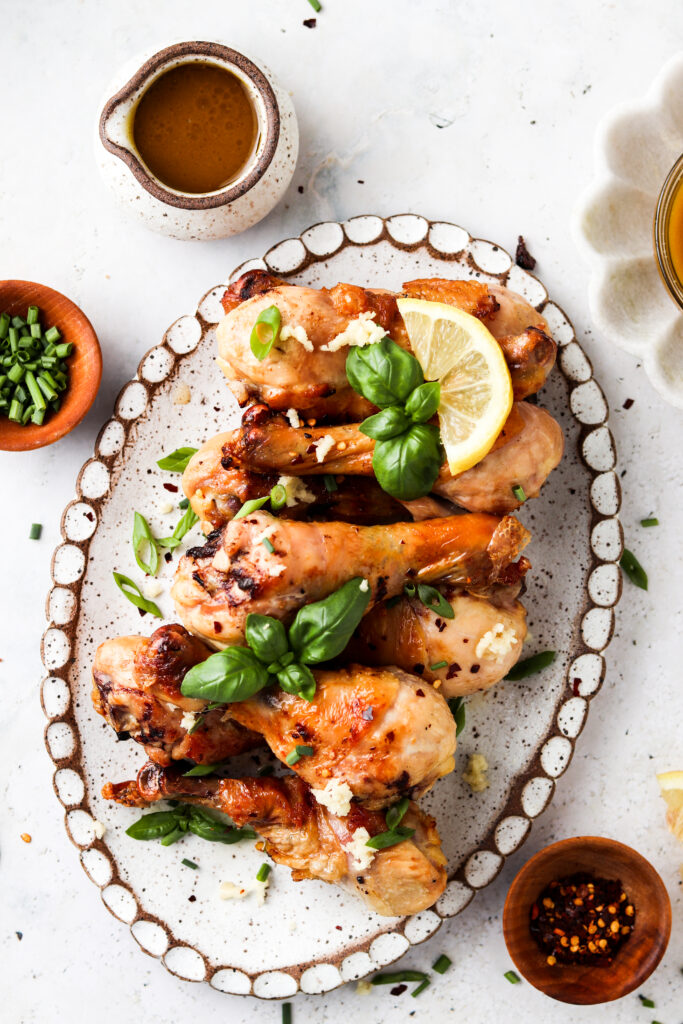 honey lemon garlic chicken drumsticks on a platter with fresh basil and lemon wedge garnish