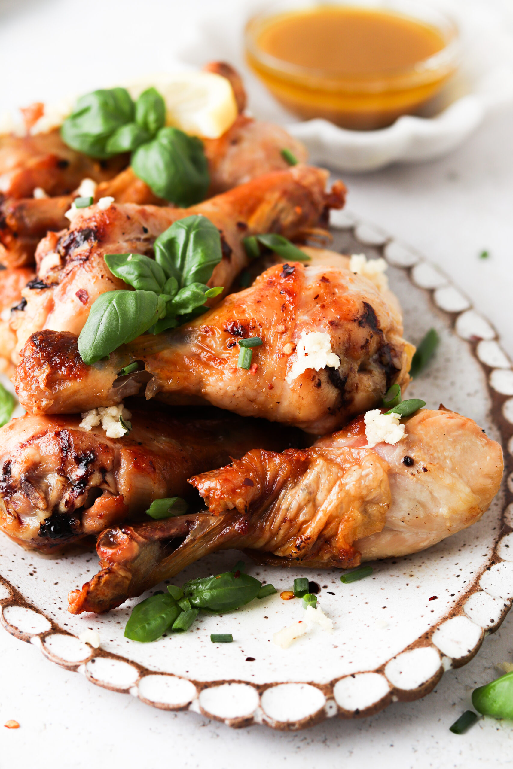 Honey lemon garlic chicken drumsticks on a platter with additional sauce in the background. 