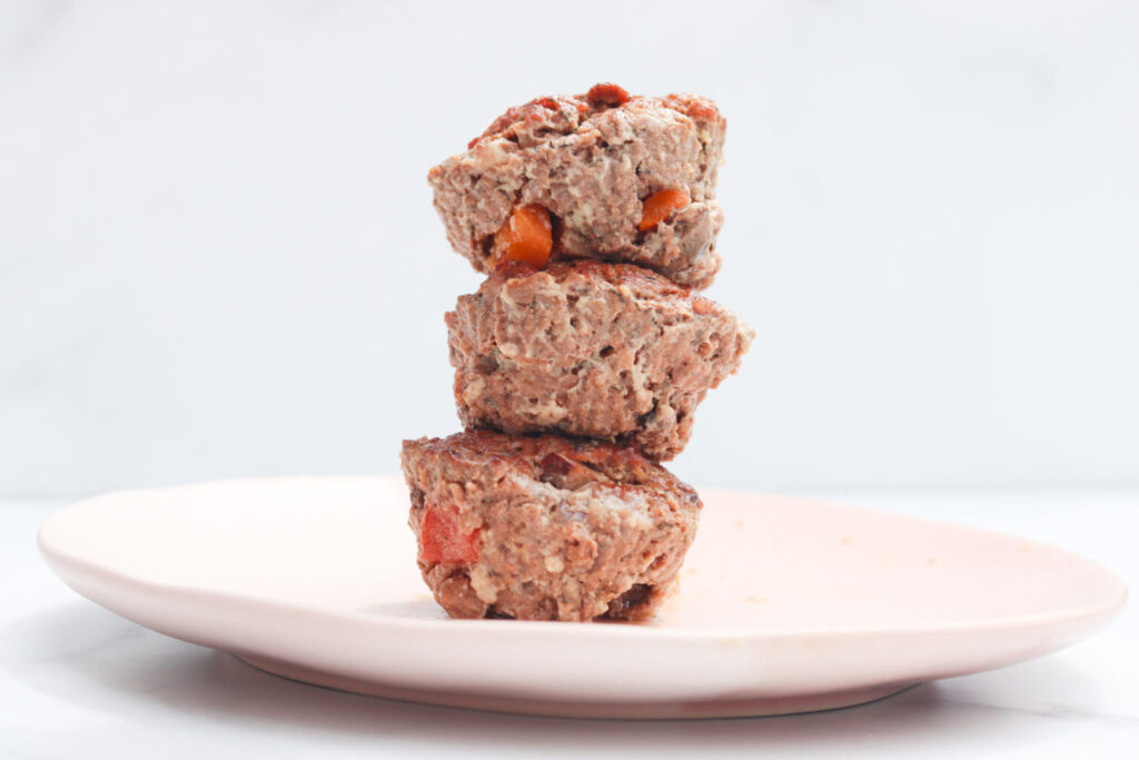 meatloaf muffins with vegetables stacked on top of each other in a tower sitting on a pale pink palte