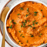 Close up photo of sweet potato mash in a bowl with chopped up chives as a garnish on top.