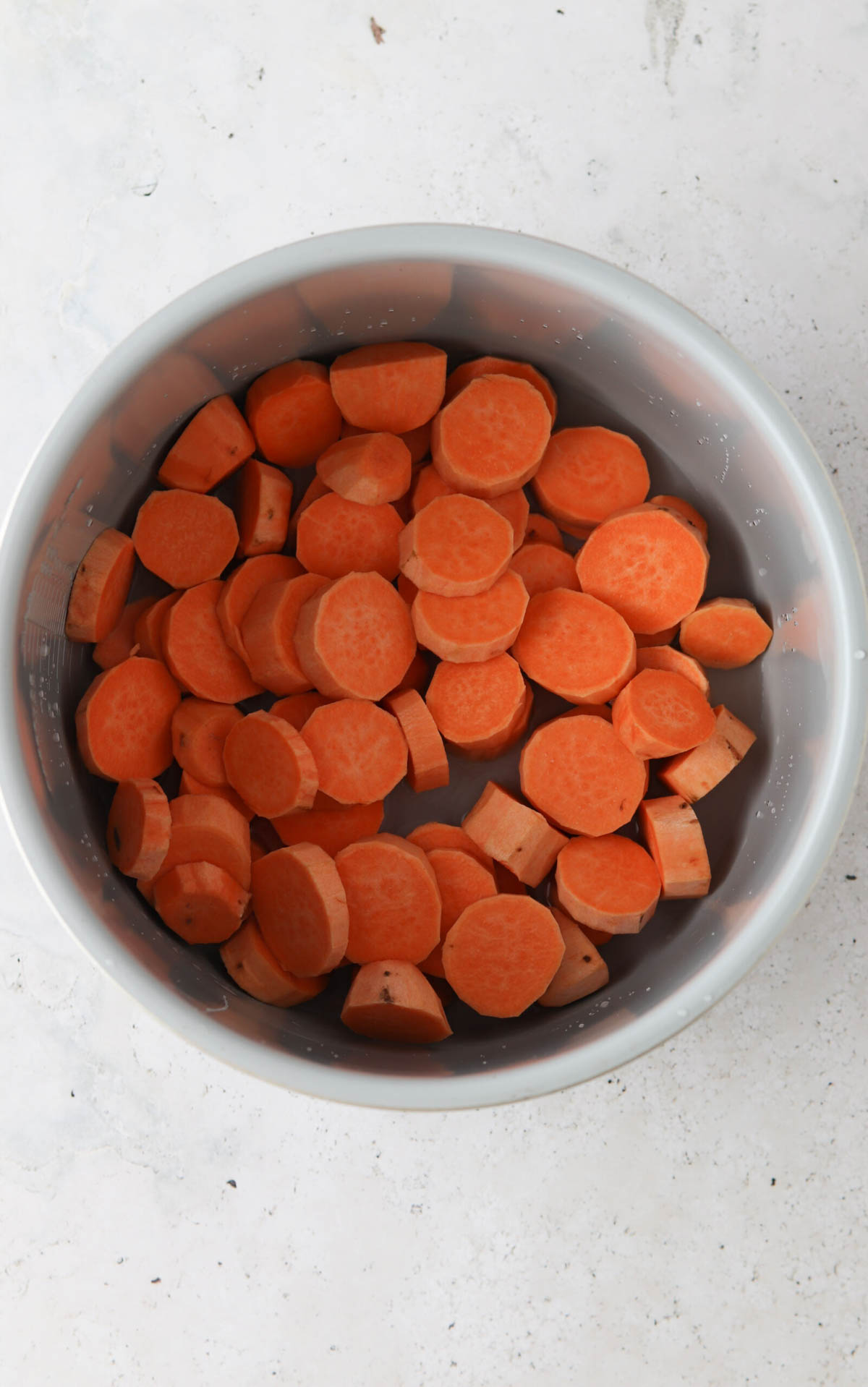 Sliced sweet potatoes in a pressure cooker base.