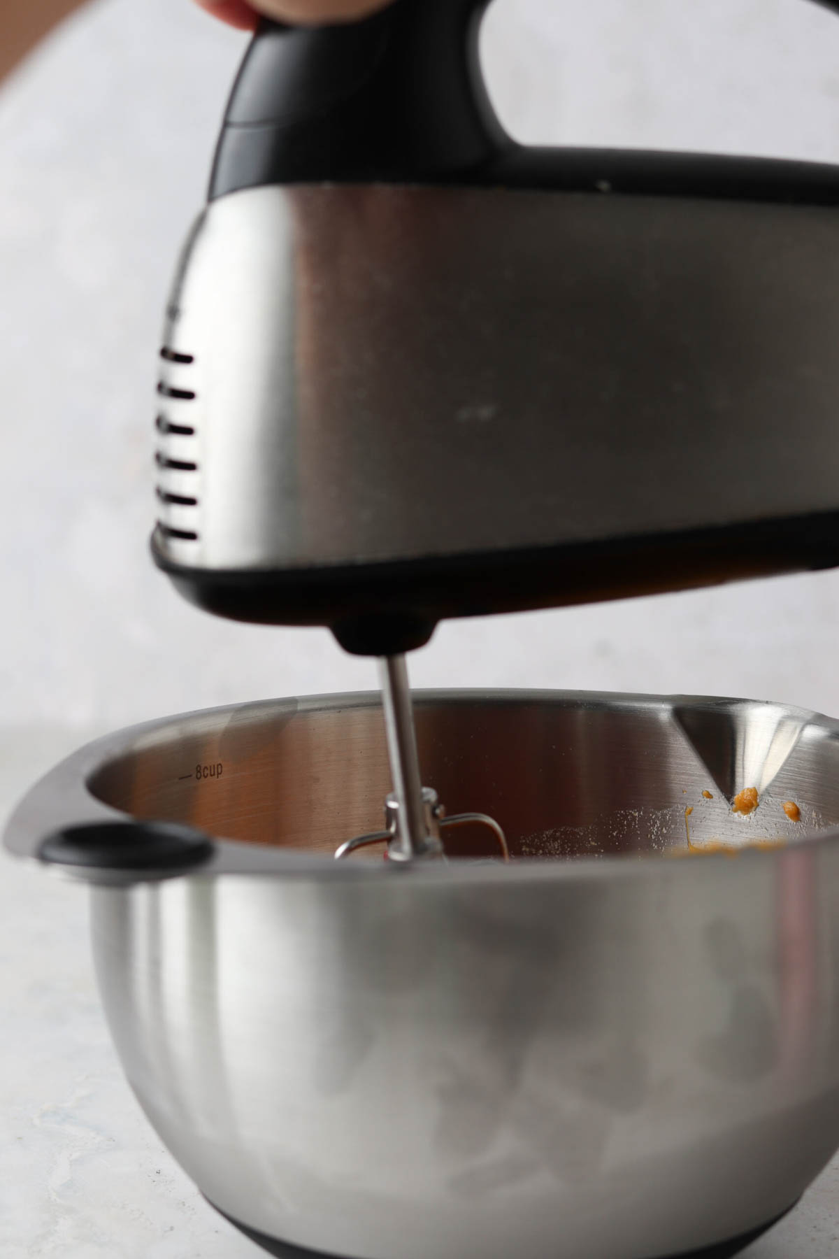 Hand mixer in a metal mixing bowl filled with sweet potatoes.