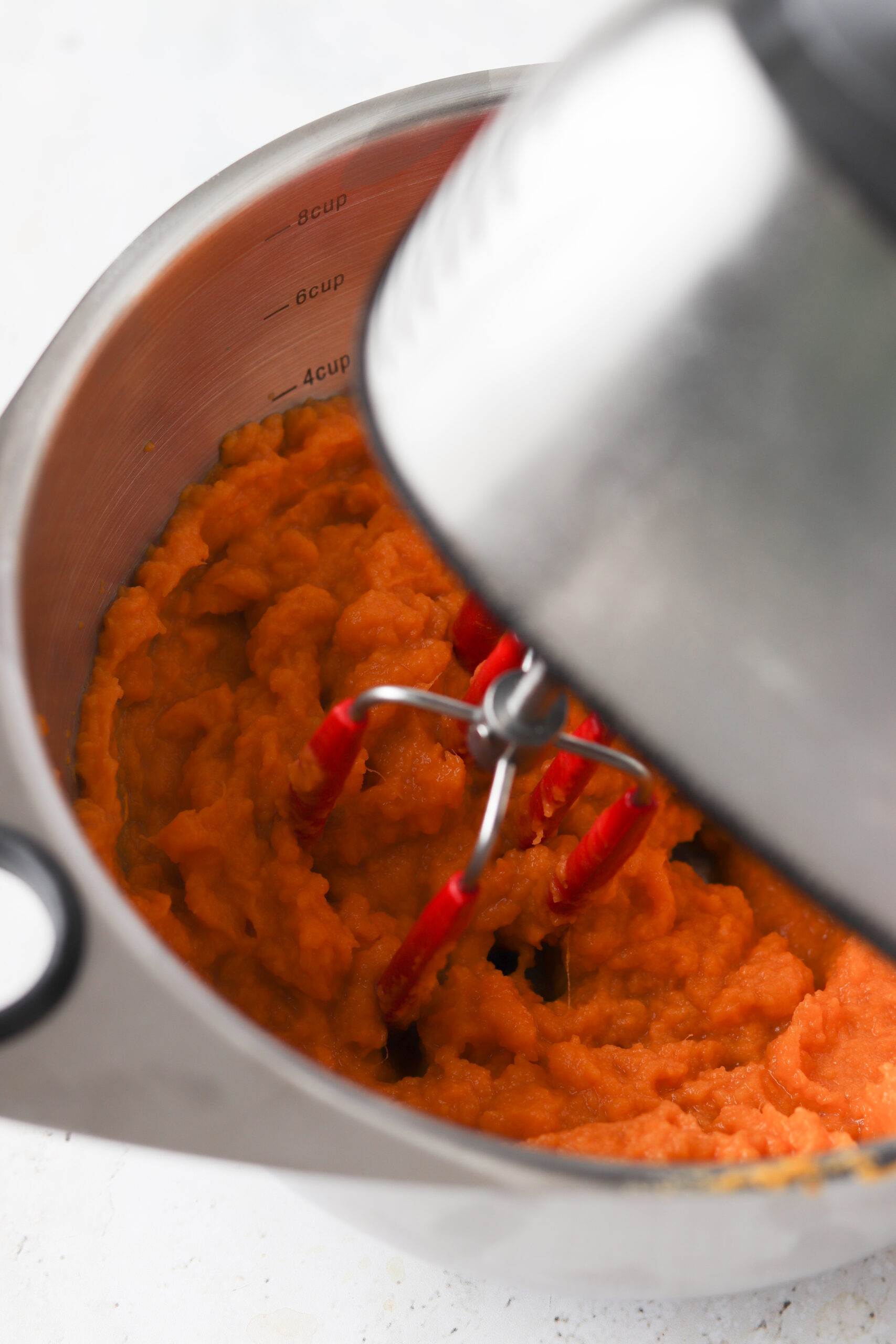 Stainless steel hand food processor over a stainless bowl with mashed up sweet potatoes. 