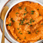 Vegan sweet potato mash in a bowl with fresh green herbs and a gold spoon.